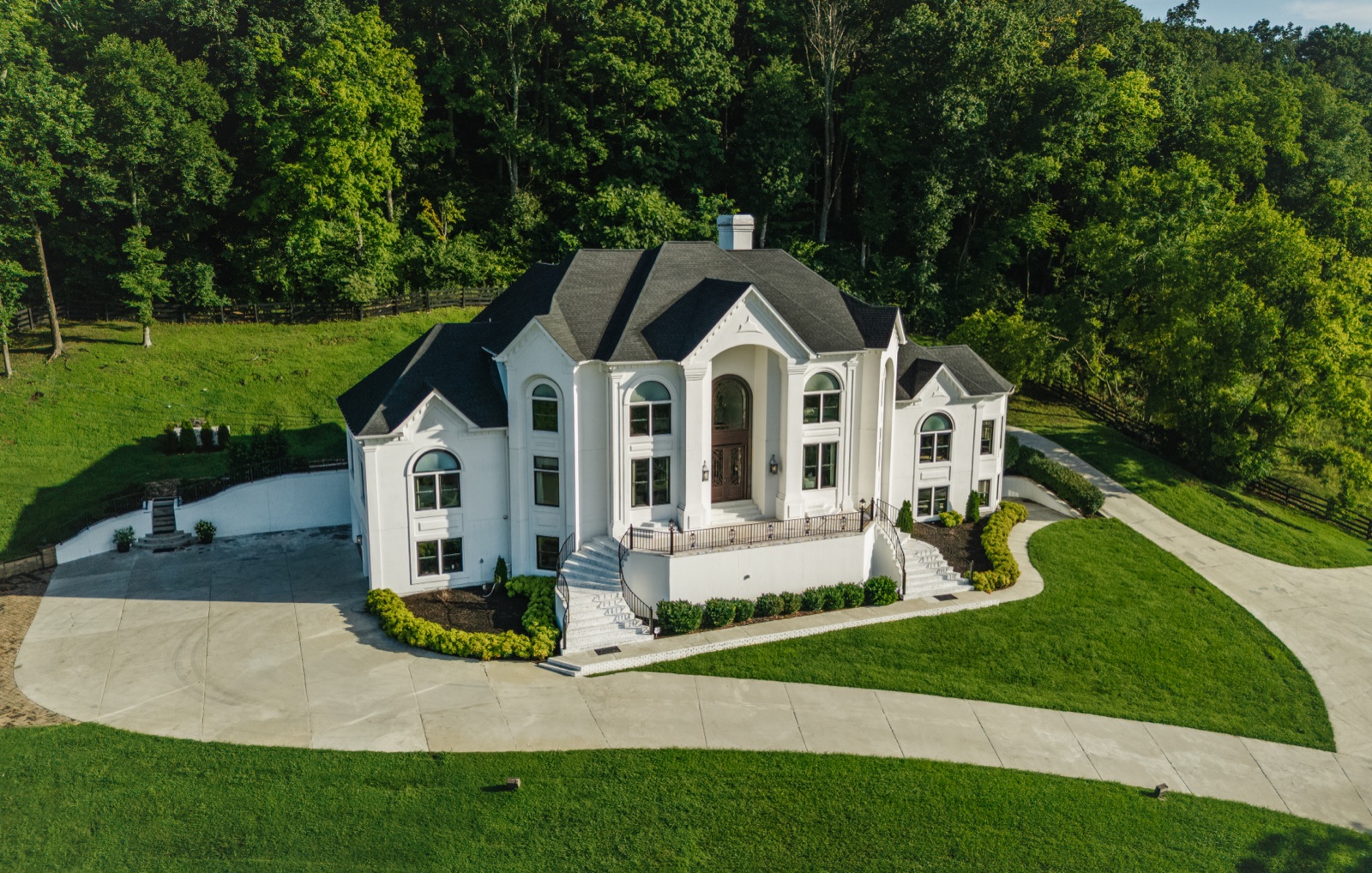 The front elevation from the air: twin curved staircases, the iron door, and woods holding the hilltop to itself.