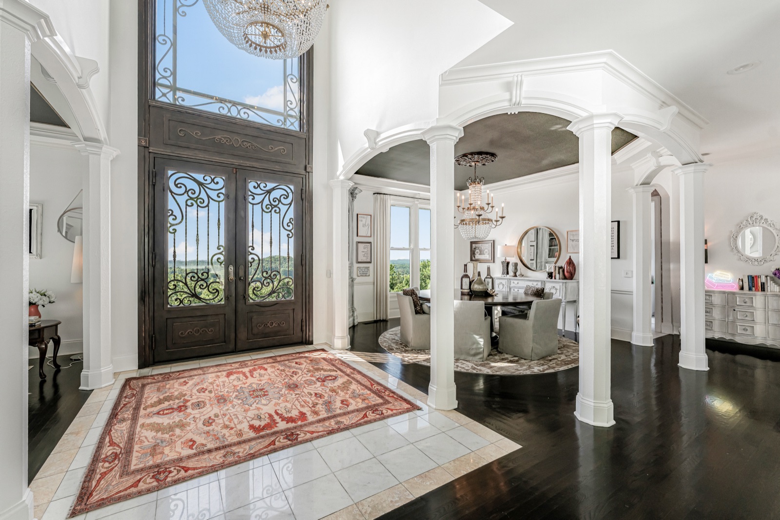 The entry foyer from the open iron front door, columns framing the county view beyond.
